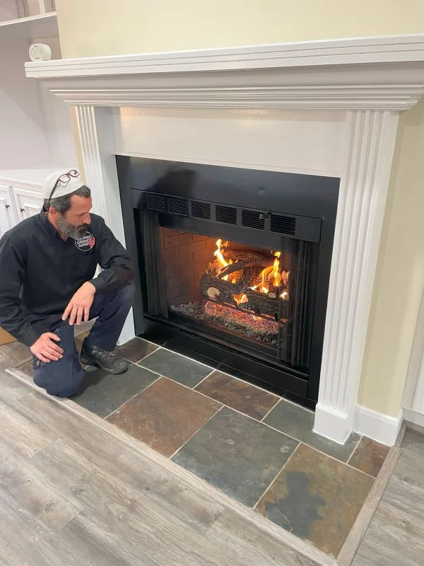 Man kneeling in front of white fireplace with burning logs, inspecting hearth area in residential home.