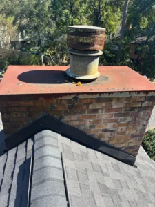 Old chimney top with round metal vent and weathered red brick