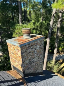 Weathered brick chimney with rust on the metal top and vent pipe