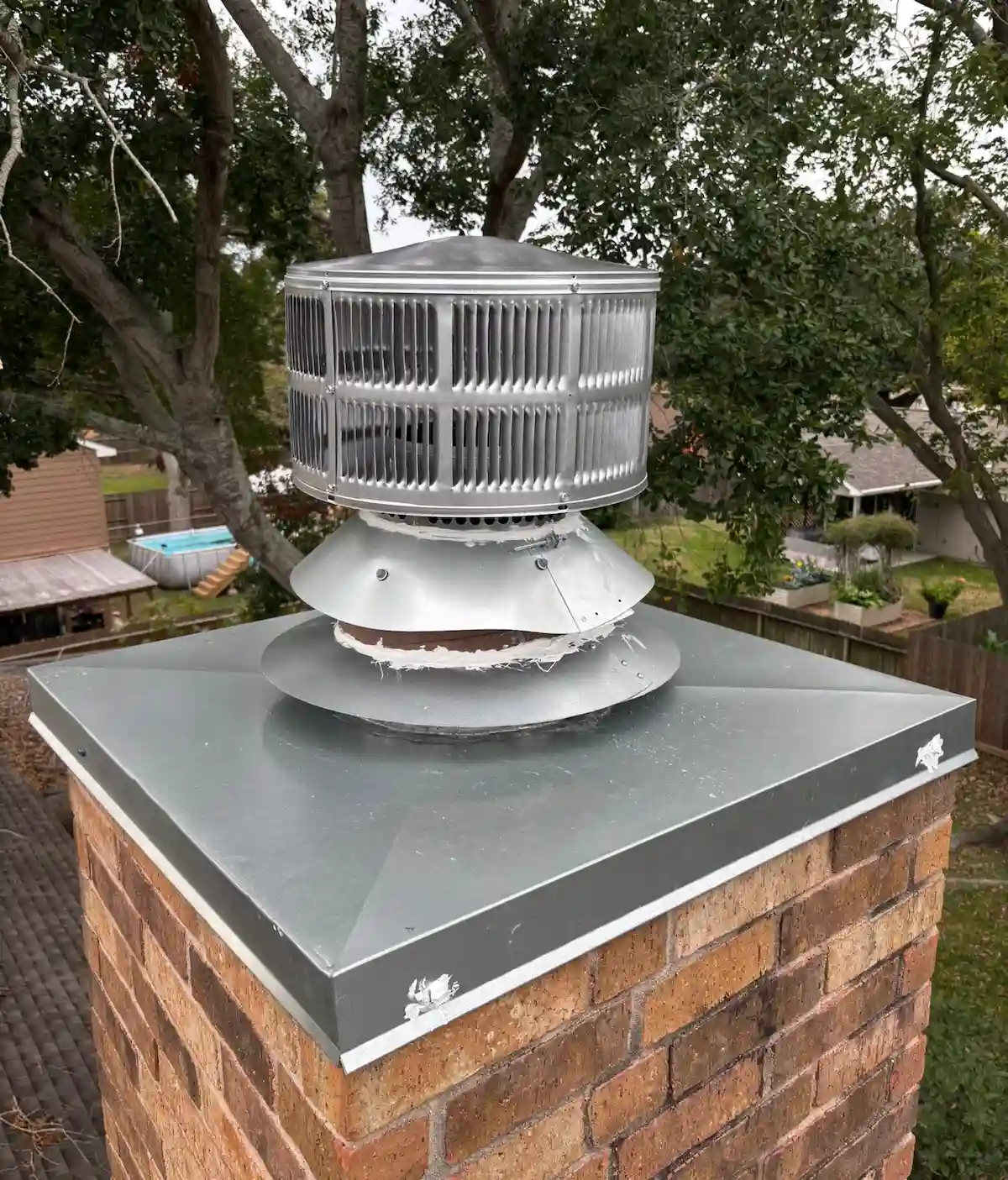 New stainless steel chase pan and chimney cap installed by Texas Chimney LLC on a brick chimney.