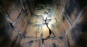 Interior view of a chimney flue showing severe cracks and fractures in the clay tile liners.