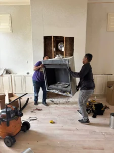 two workers installing or removing a manufactured fireplace unit as part of a home renovation project