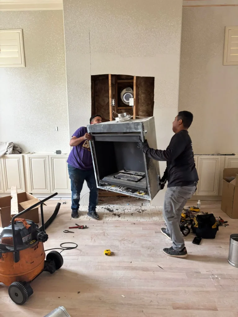 two workers installing or removing a manufactured fireplace unit as part of a home renovation project