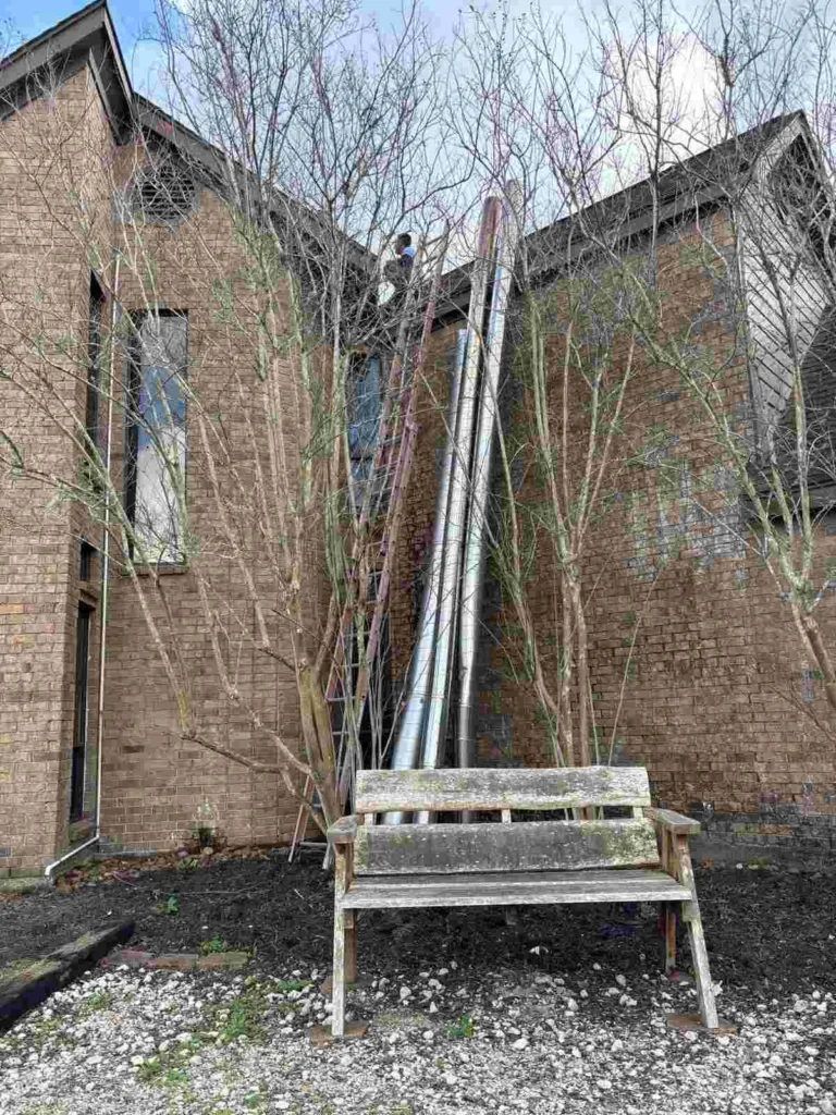 A wooden bench, ladders, and metal pipes are visible in the foreground.