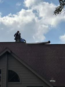 roofers performing work on an asphalt shingle roof, likely a repair or installation of a ventilation pipe.