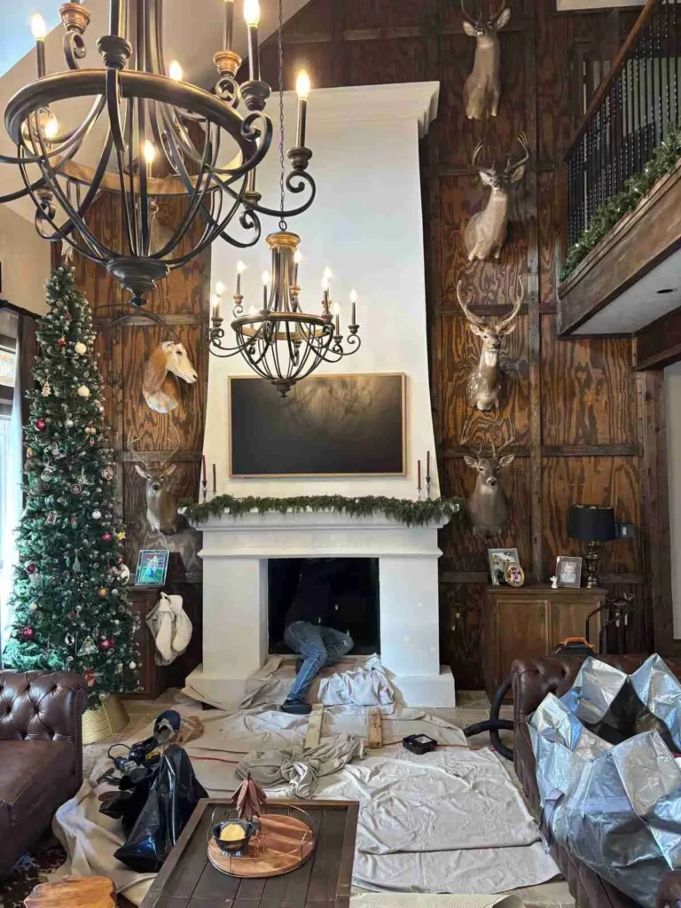 Someone appears to be working near the fireplace, which is surrounded by drop cloths, suggesting ongoing work or cleaning.