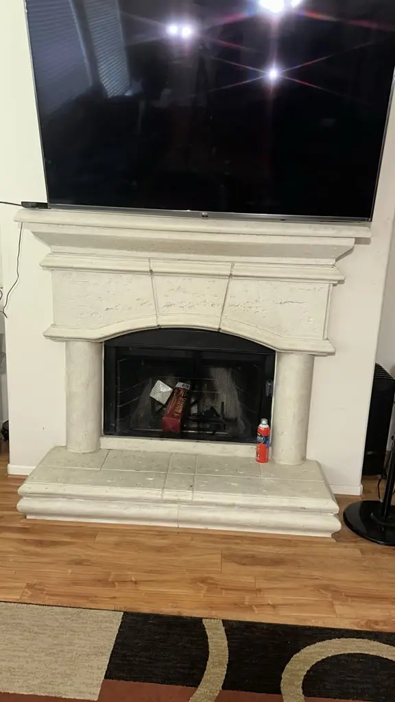 Elegant white stone fireplace mantel and hearth in a living room with a television mounted above the fireplace.